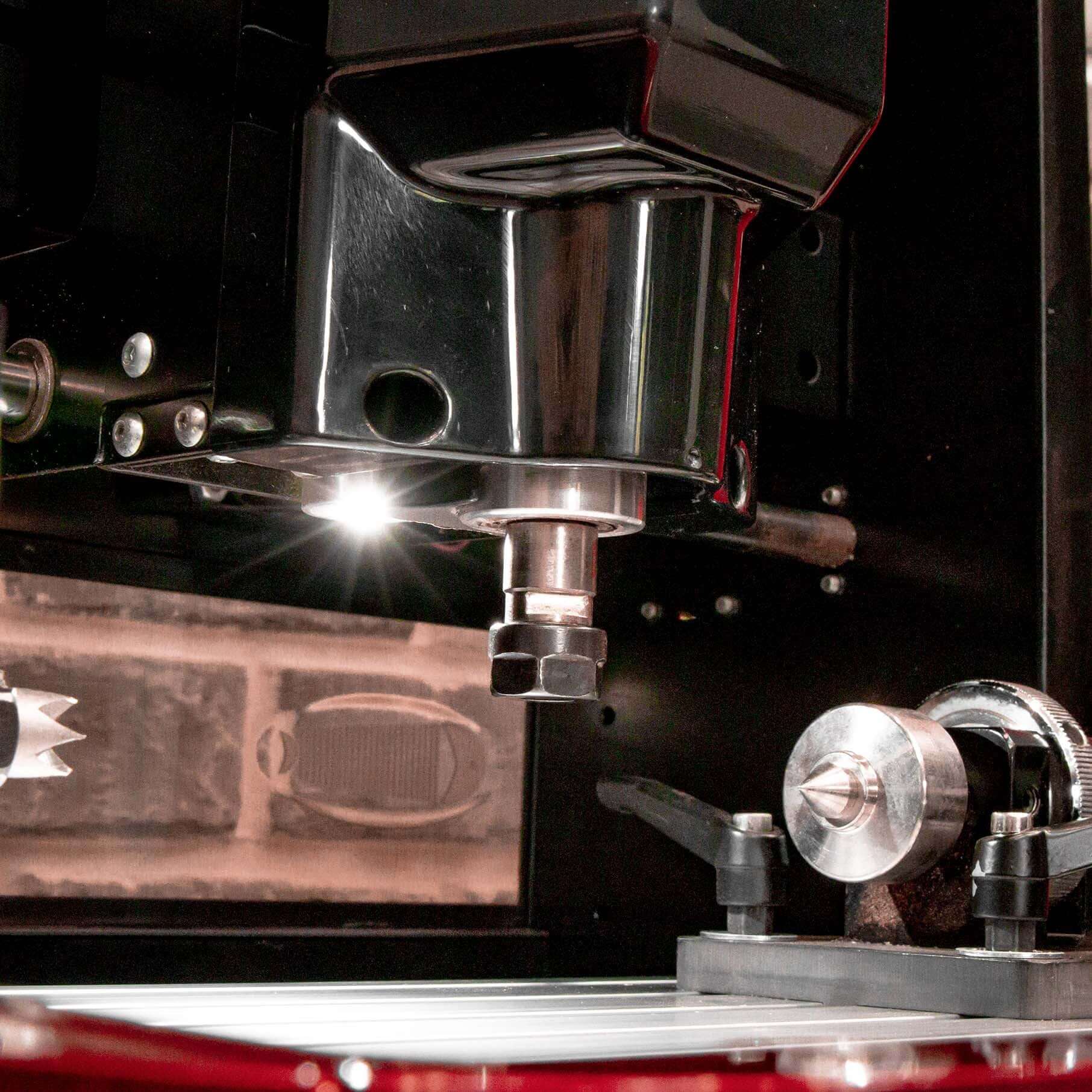 Close-up of mini CNC machine spindle and clamping system during engraving process, with reflective metal components and precision tooling visible.