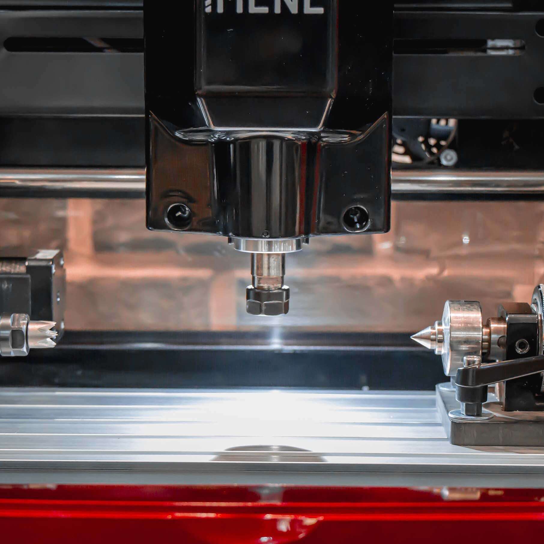 Front close-up of IMCNC mini CNC spindle and rotary axis attachment on the engraving bed, designed for precision cylindrical engraving.