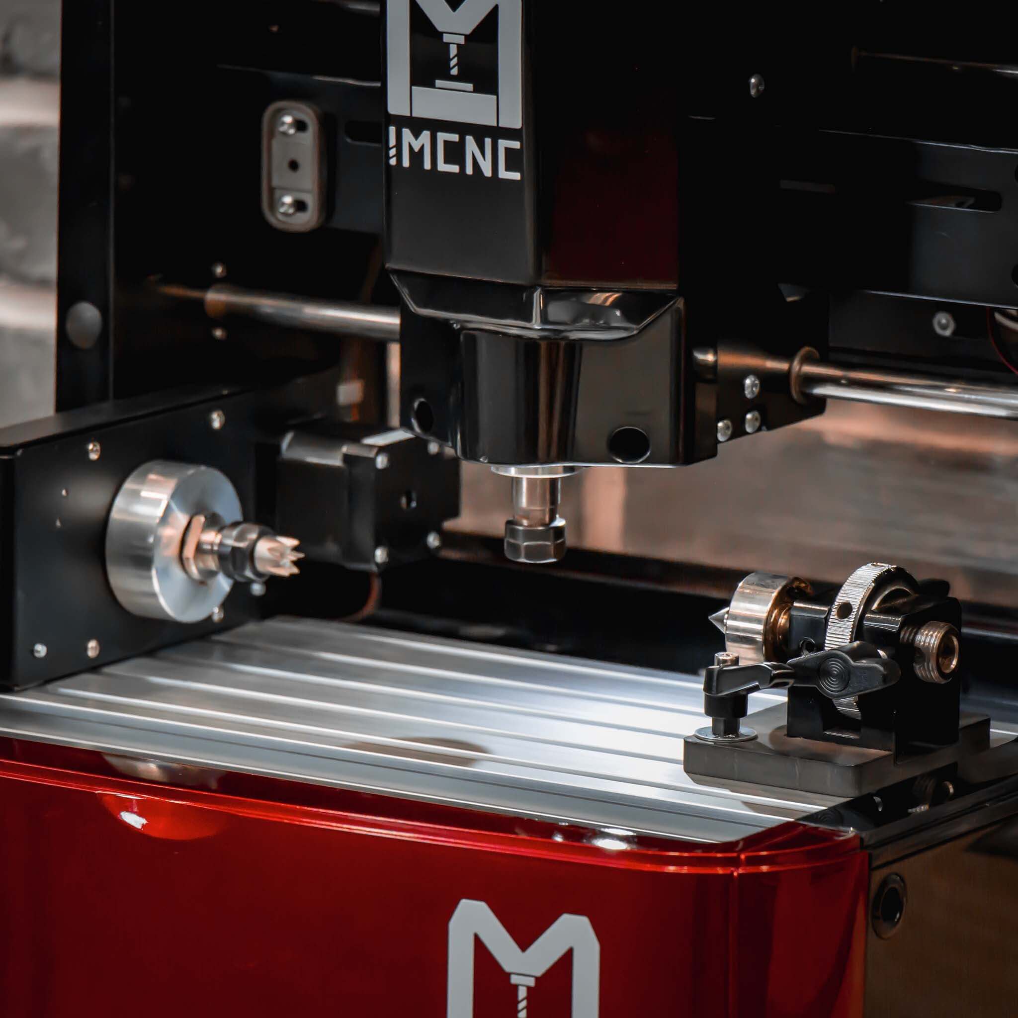 Close-up of IMCNC mini CNC engraving machine with red base, visible spindle, rotary attachment, and precision clamps on the engraving bed.