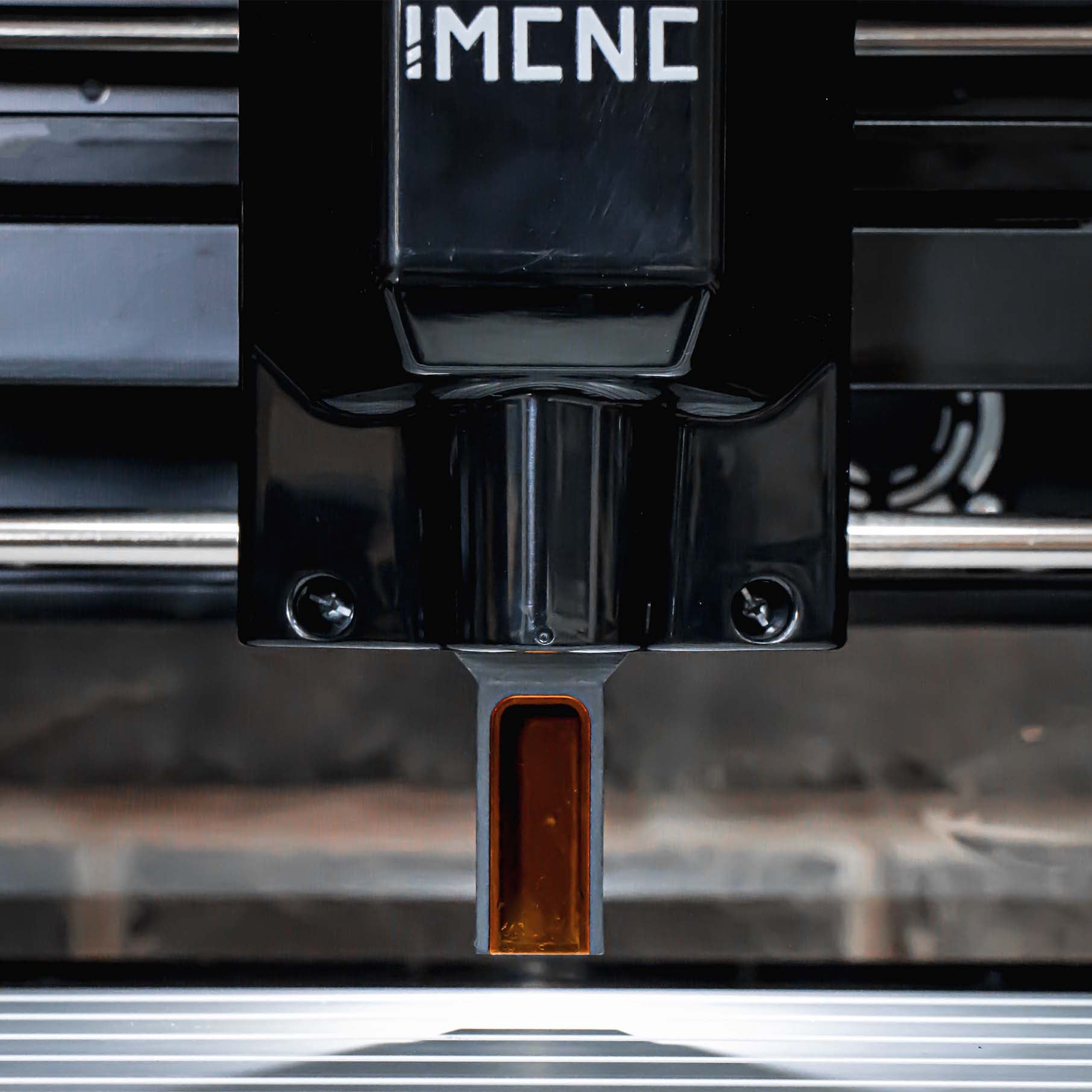 Close-up of IMCNC mini CNC machine laser spindle head with protective cover, positioned above metal engraving bed.