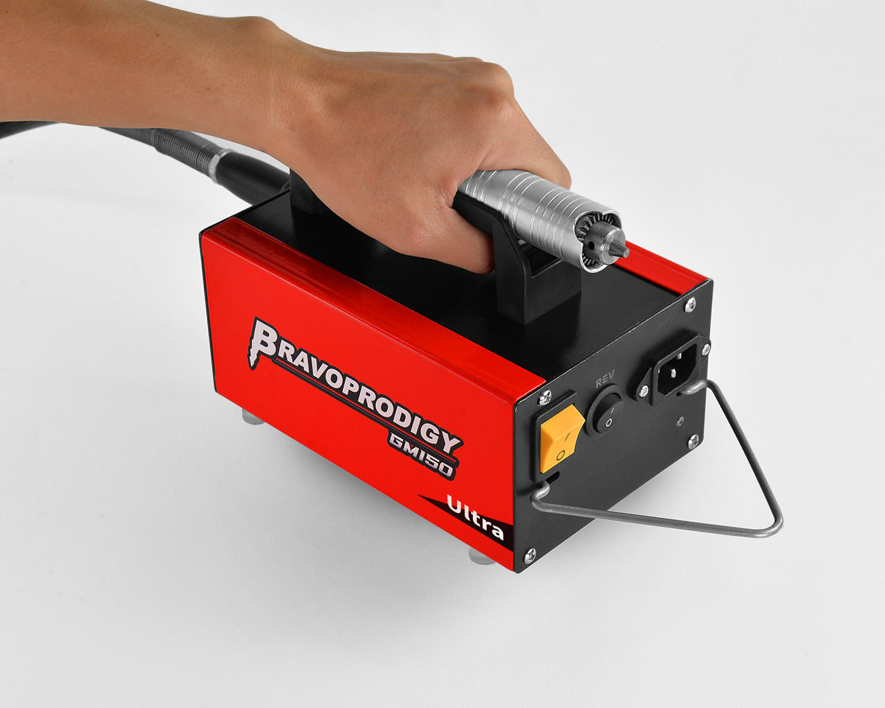 A close-up of a person holding the BRAVOPRODIGY GM150 Ultra rotary tool unit by its handle, showing the power switch, REV button, and handpiece resting on top.