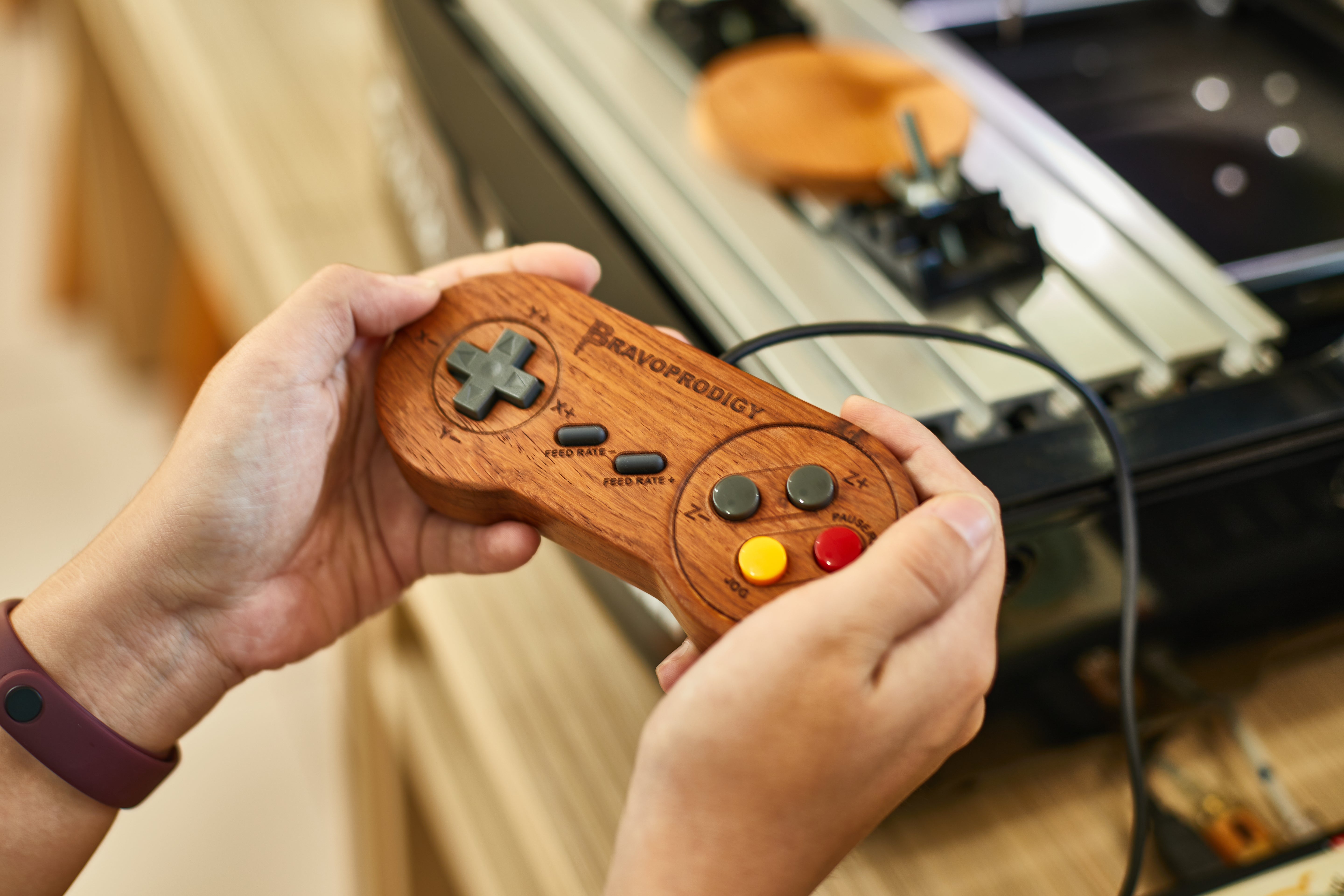 Hand holding a handcrafted wooden game controller engraved with ‘BRAVOPRODIGY’, featuring colorful retro buttons, made with precision CNC machining