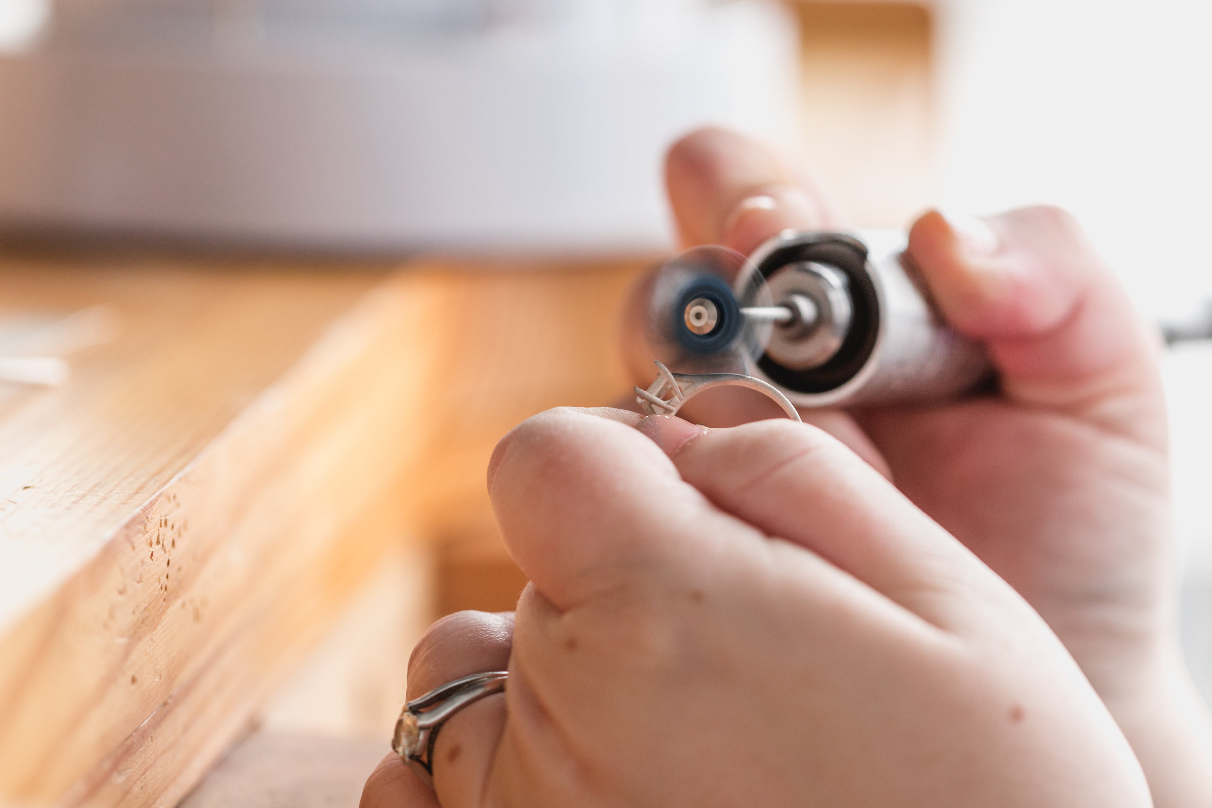 Close-up of a person using a rotary tool with a polishing or grinding bit to shape or smooth a small metal ring, held in their hand.