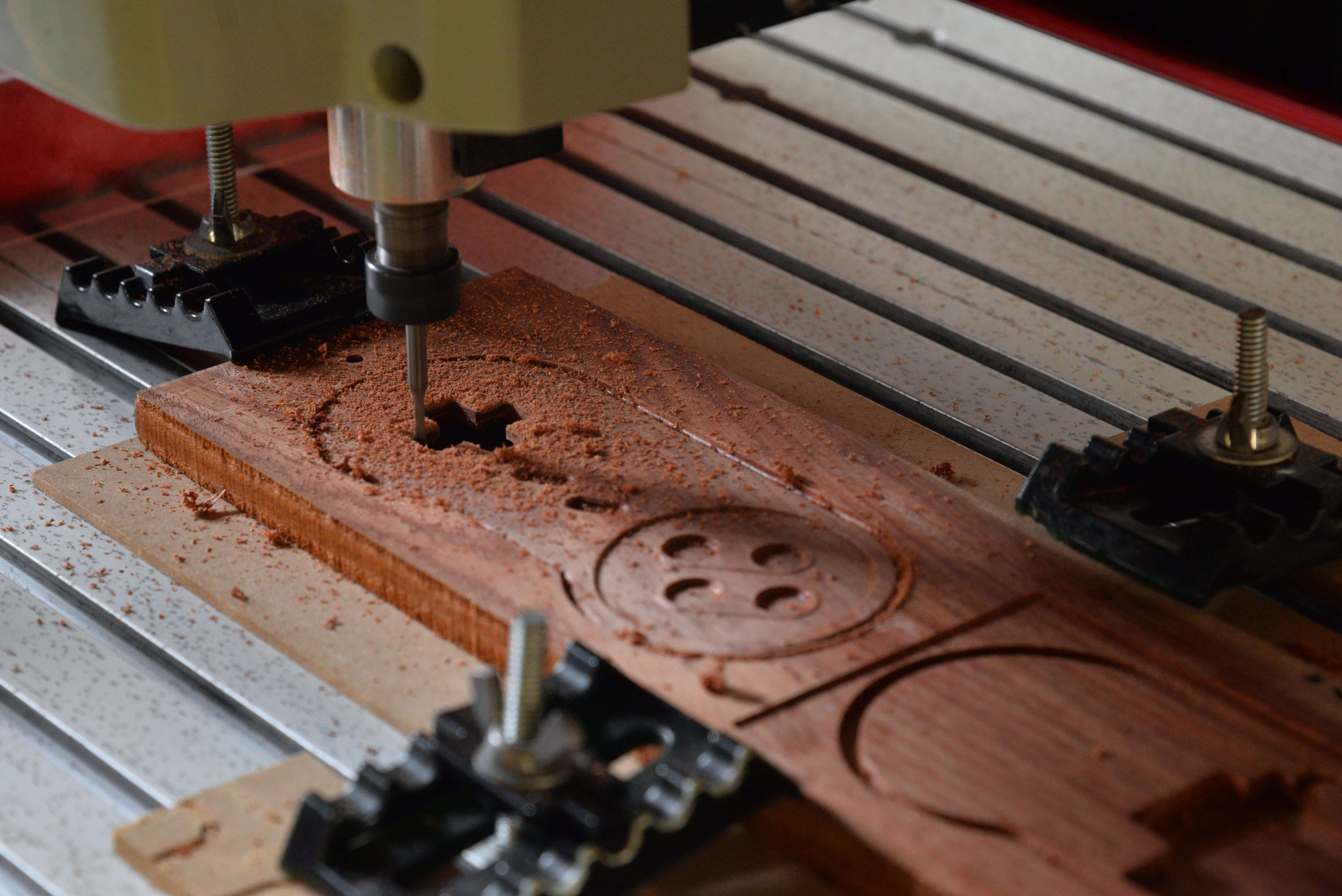 CNC mini engraver cutting custom patterns and holes on wooden board with clamps for stable woodworking engraving.